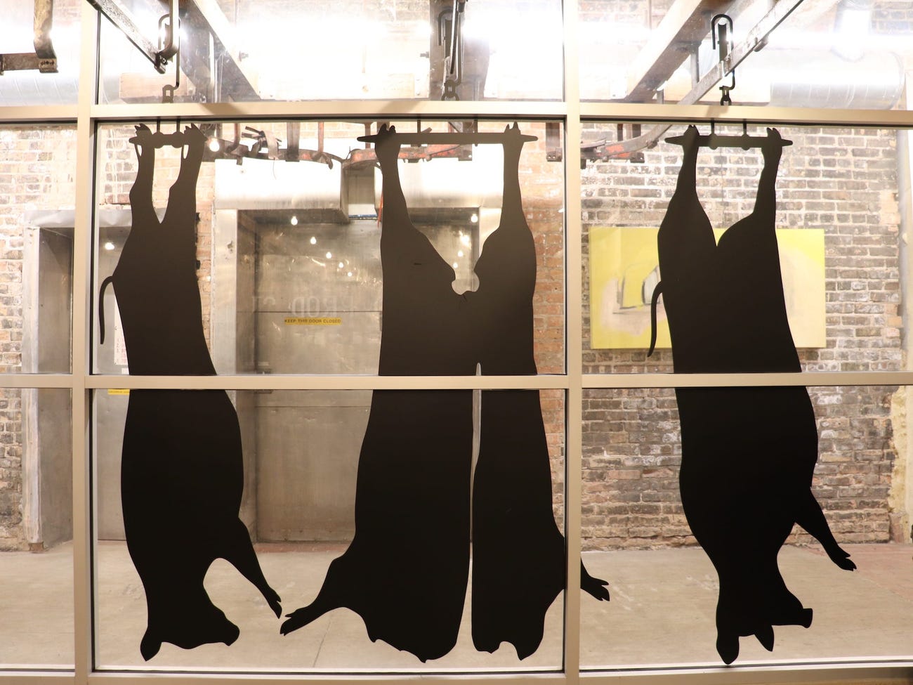black decals on windows portray cow and pig carcasses hanging by their rear feet on railings for processing