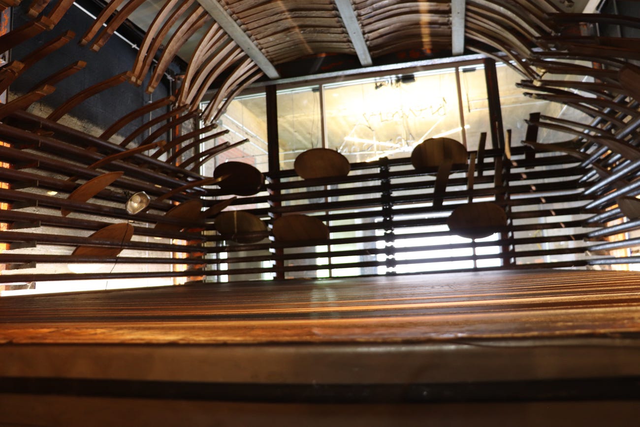 flat wooden surface fills a room with rows of pipes wrapping around the perimeter and curved wooden slats from barrels hanging on the ceiling