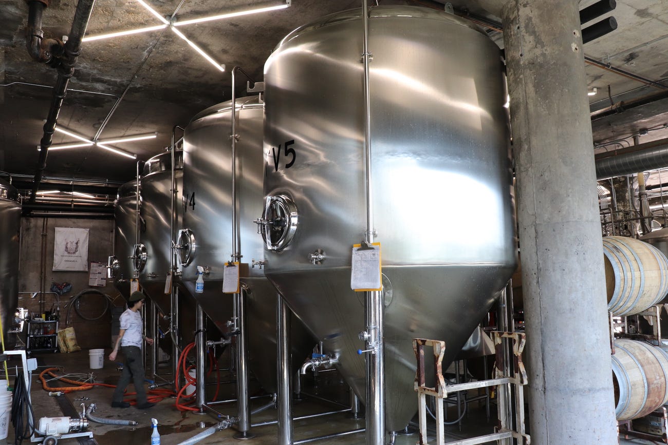 person walks beneath four large metal vats for brewing beer