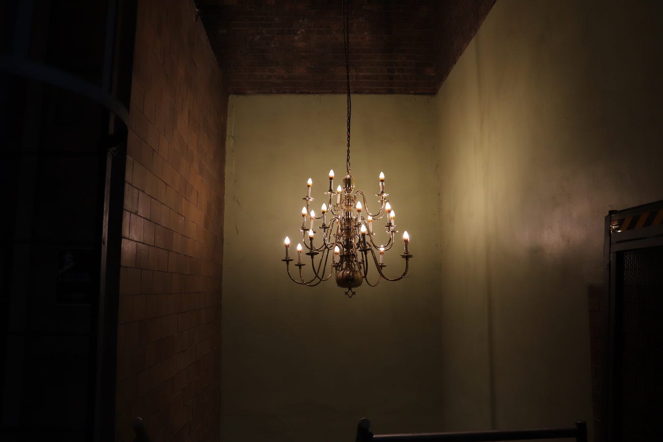 a lit chandelier hangs at the top of a dark stairwell